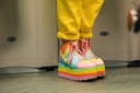 A close-up of the brightly coloured platform boots of Leah Thomas. They are rainbow coloured and feature pink laces. They match with Leah's yellow jumpsuit.