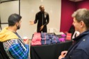 Nathaniel Okenwa smiles as he talks with conference attendees at the Twilio stand. On the table in front of him are a selection of pink and blue Twilo t-shirts. A logo on his hoodie reads, Community Hero.