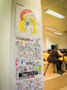A shot of the Drawnalism illustrations from the morning sessions. The illustrations are taped to the wall and depict the sessions by Jo Franchetti and Sascha Wolf in a series of infographic style cartoons. In the background the film cameras are prepared for the next sessions.