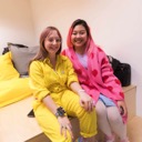 Leah Thomas and Rachel Konichiwakitty sit together at the back of the auditorium. They are both smiling happily. Leah's yellow jumpsuit complements Rachel's pink cardigan.
