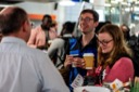 An attendee named Steve enjoys a conversation with another attendee whilst he holds a coffee cup. Another attendee is exploring the conference promotional materials.