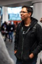 Akash Goswami stands in the foyer and smiles. His hands are in the pockets of his grey hoodie and he is wearing a backpack.
