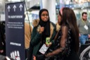 An attendee named Fatima talks with another attendee in the conference foyer. She is wearing a headscarf and holding a can of 7 Up.